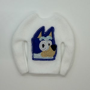 Peut inclure: Pull en polaire blanc avec un chien de dessin animé brodé en bleu et beige portant un masque bleu.