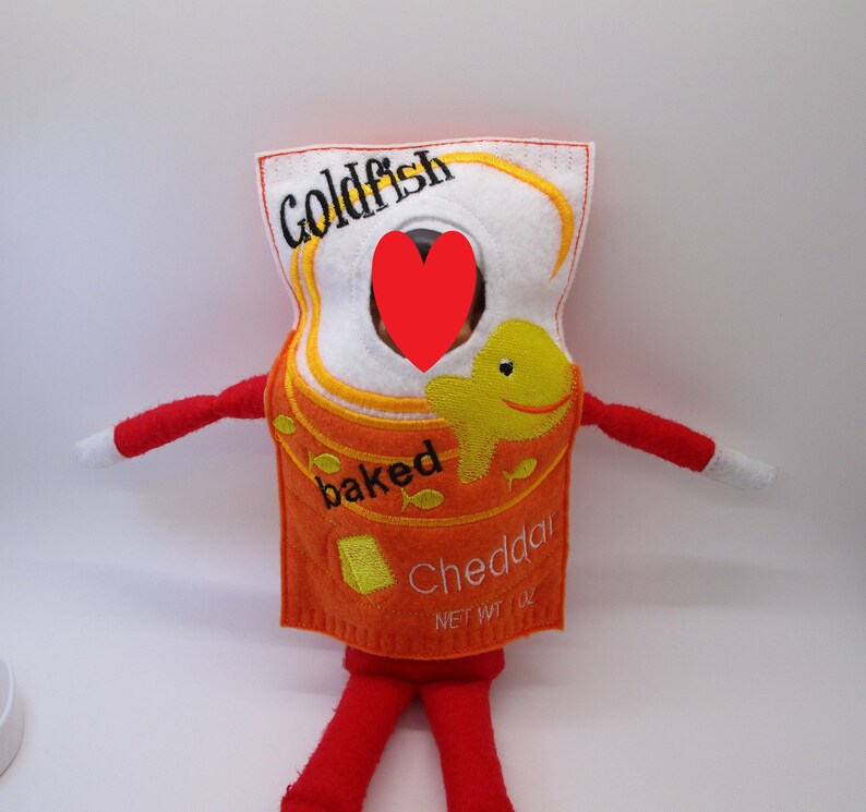 May include: A felt elf costume shaped like a box of Goldfish crackers. The box is orange and white with the words "Goldfish", "baked", and "Cheddar" on it. There is a small yellow fish illustration on the box.