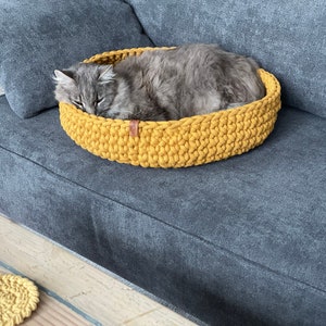 Puede incluir: Un gato gris durmiendo en una cama de gato de crochet amarillo en un sof&aacute; gris.