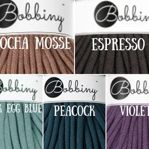 Puede incluir: Seis carretes de cuerda de algod&oacute;n en varios colores, incluyendo moca, espresso, azul huevo de pato, pavo real y violeta. Cada carrete tiene una etiqueta blanca con la palabra "Bobbiny" en letras negras y el nombre del color debajo.