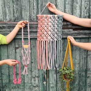 Puede incluir: Tres tapices de macram&eacute; para colgar en la pared, uno con un patr&oacute;n geom&eacute;trico rosa y azul, otro con un patr&oacute;n geom&eacute;trico rosa y blanco y otro con una cuerda amarilla. Los tapices est&aacute;n hechos con cord&oacute;n de algod&oacute;n y cuelgan de una barra de madera.