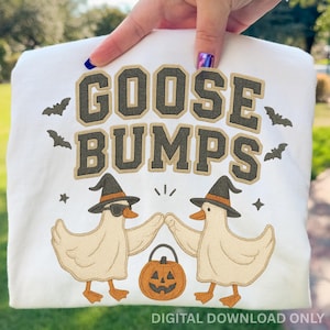May include: White sweatshirt with the text "GOOSE BUMPS" in brown and tan lettering. The design includes two cartoon geese wearing witch hats, sunglasses, and a jack-o'-lantern. Bats and stars surround the text and geese. "DIGITAL DOWNLOAD ONLY" is at the bottom.