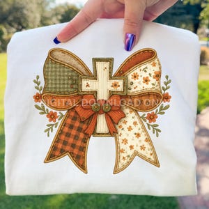 May include: White sweatshirt featuring a cross design with a bow. The bow has a plaid pattern, floral print, and solid orange sections. The cross is cream-colored with a stitched border. The design includes the text "DIGITAL DOWNLOAD ON".