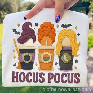 May include: White t-shirt featuring a colorful design of three stylized coffee cups, each representing a character from the movie "Hocus Pocus." The cups have different hair styles and are decorated with witchy symbols. The text "HOCUS POCUS" is below the cups.