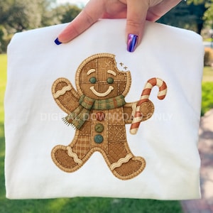 Może przedstawiać: Biała bluza z nadrukiem piernikowego ludzika. Piernikowy ludzik jest brązowy, ma zielony szalik i trzyma laskę cukrową. Projekt zawiera tekst "DIGITAL DOWNLOAD ONLY".