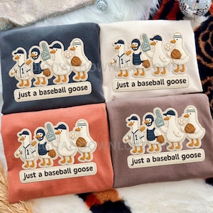 May include: Four long-sleeved shirts in various colors: navy, cream, coral, and brown. Each shirt features an embroidered design of baseball-playing geese with the text "just a baseball goose" below the geese.