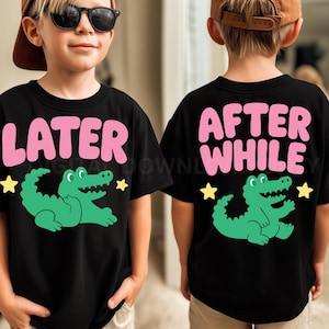 以下が含まれることがあります： 前面に「LATER」、背面に「AFTER WHILE」と書かれたピンク色の文字のデザインが施された黒いTシャツ。各シャツには緑色のワニのグラフィックと黄色の星のアクセントが付いています。子供向けにデザインされたシャツです。