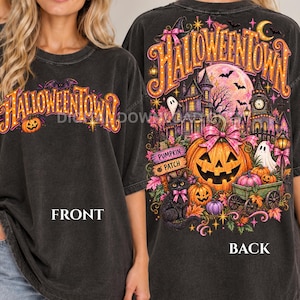 May include: A charcoal gray t-shirt featuring a Halloweentown graphic. The front displays the text Halloweentown with a pumpkin. The back shows a detailed scene with a haunted house, a large jack-o'-lantern, a black cat, and a ghost.