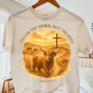 May include: Cream-colored t-shirt featuring a watercolor design with a Highland cow, cross, and the text "Follow the Word, Not the Herd." The phrase "Digital Download Only" is also present, along with the Bible verse Isaiah 8:11-13.