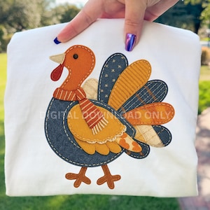 May include: White sweatshirt featuring a colorful turkey applique. The turkey has an orange head, a red wattle, and a patterned scarf. The wings are made of various patterned fabrics in blue, yellow, and beige. The text "DIGITAL DOWNLOAD ONLY" is printed on the sweatshirt.
