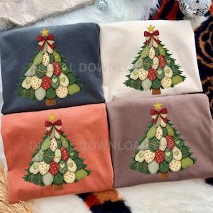 Könnte beinhalten: Vier gefaltete Sweatshirts in verschiedenen Farben: Marine, Creme, Koralle und Braun. Jedes hat ein gesticktes Weihnachtsbaumdesign mit Stern, Schleife und dekorativen Ornamenten. Die Bäume haben ein Patchwork-Design mit grünen, roten und cremefarbenen Elementen.