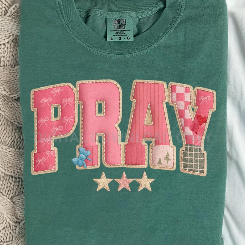 May include: A teal green sweatshirt with the word "PRAY" in pink, appliqued letters. The letter "P" has pink bows, the "R" has vertical stripes, the "A" has a blue flower, and the "Y" has a checkered pattern. Three gold stars are below the word.