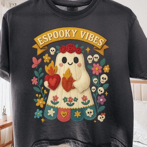 Op de afbeelding: Donkergrijs t-shirt met een kleurrijke afbeelding van een spook met een hart en een vlam. Het spook is omringd door bloemen, schedels en de tekst "ESPOOKY VIBES" in een banner. Het ontwerp heeft een Halloween-thema.