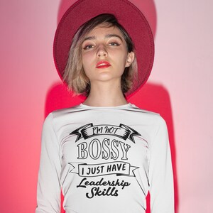 May include: A white long-sleeve shirt featuring the black text I'M NOT BOSSY I JUST HAVE Leadership Skills, paired with a dark red wide-brimmed hat and a matching dark red skirt, creating a coordinated outfit with a bold graphic design.