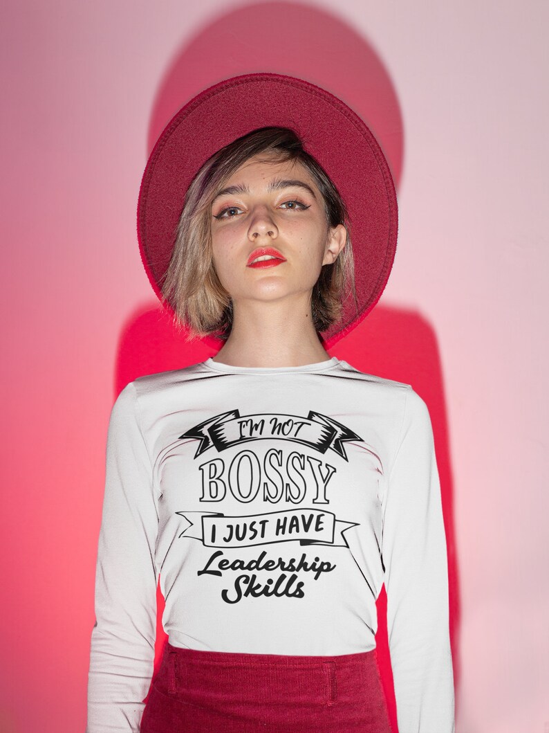 May include: A white long-sleeve shirt featuring the black text I'M NOT BOSSY I JUST HAVE Leadership Skills, paired with a dark red wide-brimmed hat and a matching dark red skirt, creating a coordinated outfit with a bold graphic design.