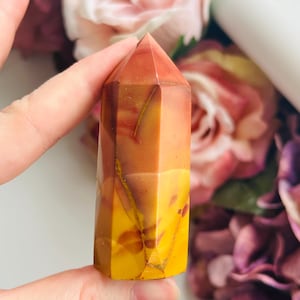 May include: A polished, six-sided crystal tower featuring a smooth, multi-coloured surface with distinct bands of warm yellow, deep orange, and earthy red tones, showcasing natural mineral inclusions and a pointed, faceted top section.