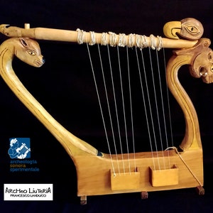 May include: A wooden lyre with a carved animal head on each end. The lyre has 10 strings and is made of light brown wood. The lyre is a musical instrument used in ancient Greece.