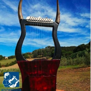 May include: A black and red lyre with a wooden frame and a soundboard. The lyre has a set of strings and is decorated with a carved design. The lyre is set against a blue sky with white clouds.