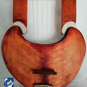 May include: A wooden lyre with a heart-shaped body and seven strings. The instrument has a warm, reddish-brown finish with a lighter wood accent at the top and sides. The logo of ArcheoLiuteria is visible at the bottom.