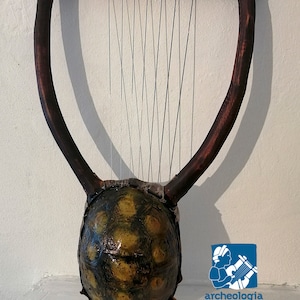 May include: A wooden lyre with a turtle shell resonator. The lyre has a wooden frame with a row of tuning pegs and strings. The turtle shell is brown and yellow with a pattern of scales. The lyre is a musical instrument used in ancient Greece.