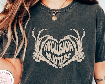 May include: A dark grey t-shirt with a graphic of two skeleton hands forming a heart shape with the text "Inclusion Matters" inside.