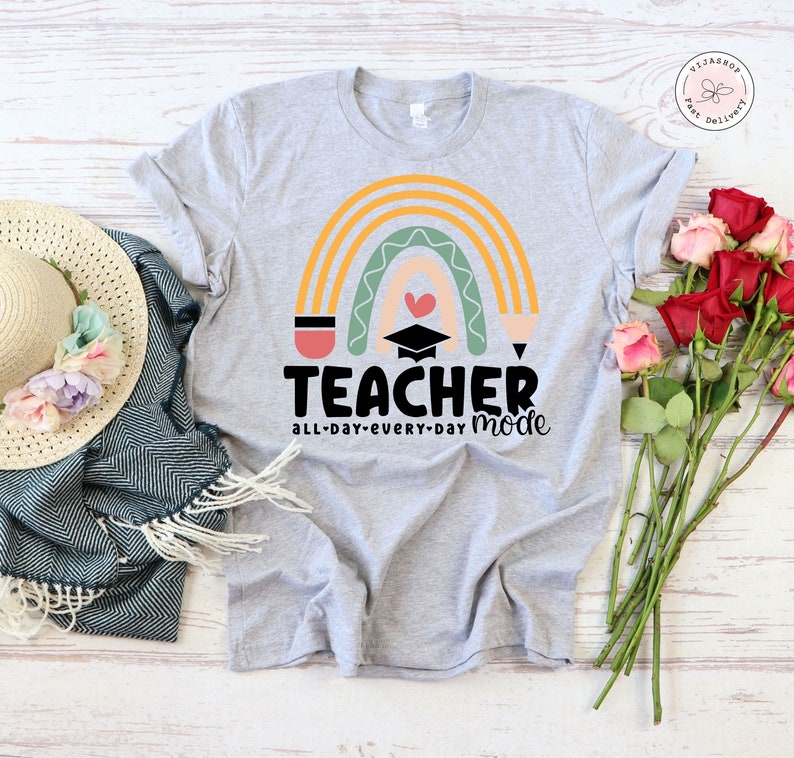 Pu&ograve; includere: Una maglietta grigia con un design a arcobaleno e il testo "TEACHER all-day-every-day mode". L'arcobaleno &egrave; composto da strisce gialle, arancioni, verdi e rosa. Al centro dell'arcobaleno c'&egrave; un cappello da laurea e un cuore.