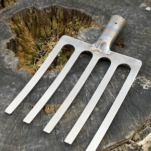 Könnte beinhalten: Ein silbernes Gartenwerkzeug aus Metall mit fünf Zinken. Das Werkzeug liegt auf einem Baumstumpf.