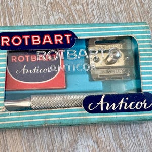 May include: A vintage Rotbart Anticor safety razor set in a blue and white striped cardboard box. The set includes a silver-toned metal razor handle with a textured grip and a matching metal razor head, displayed in a blue plastic insert.