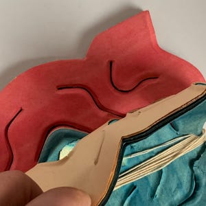 May include: A multi-layered paper mask with a red, blue and tan colour scheme. The mask is folded in half and the layers are visible. The mask is decorated with a wavy pattern.
