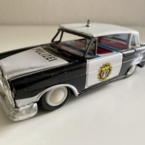 Könnte beinhalten: Ein schwarzes und weißes Spielzeug-Polizeiauto mit rotem und blauem Innenraum. Das Auto hat ein "POLIZEI"-Schild auf der Motorhaube und ein Wappen an der Seite.