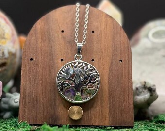 May include: A silver-toned pendant necklace featuring a circular frame with a cutout tree design. The tree is inlaid with iridescent, multicolored abalone shell fragments. The pendant hangs from a delicate silver-toned chain.