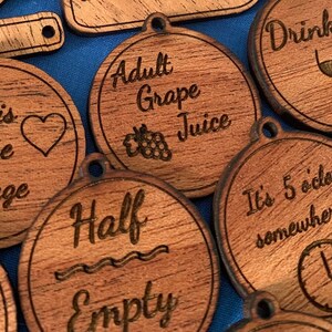 Pode incluir: Uma coleção de ornamentos de madeira com tema de vinho com vários ditados, incluindo "O vinho é a minha linguagem do amor", "Suco de uva para adultos", "Continue servindo", "Meio vazio", "Beba-me", "São 5 horas em algum lugar", "Tomar decisões", e "As meninas apenas".