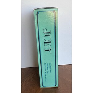 Peut inclure: Une bo&icirc;te rectangulaire haute avec un fond vert d'eau et une bordure vert fonc&eacute;. Le mot "JOEY" est imprim&eacute; dans une police stylis&eacute;e. Le texte ci-dessous indique "Cheveux enracin&eacute;s, Yeux endormis, Bras et jambes mobiles."