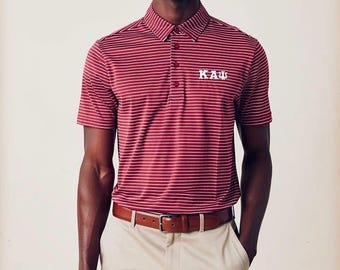 Op de afbeelding: Bordeauxrood en wit gestreept poloshirt met de Griekse letters KAI geborduurd op de borst. Het shirt wordt gecombineerd met een kaki broek en een bruine leren riem. Een klassieke, preppy stijl.