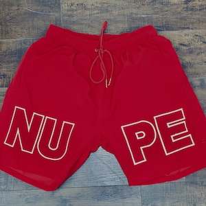 May include: Red athletic shorts with white "NUPE" lettering.
