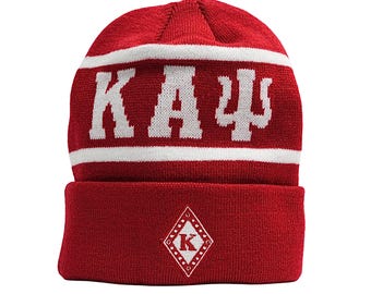 Puede incluir: Gorro de punto rojo con una franja blanca y el texto "KAU" en blanco. El gorro también tiene un pequeño diamante blanco con una "K" en el interior en la parte delantera.