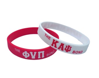 May include: Two silicone bracelets, one red and one white. The red bracelet has the text "THE ΦΥΠ BOND" in white lettering. The white bracelet has the text "THE ΚΑΨ BOND" in red lettering.