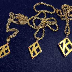 May include: Three gold necklaces with diamond-shaped pendants featuring a geometric design. Each pendant has a red gemstone in the center.
