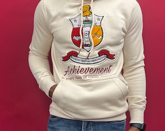 Op de afbeelding: Een crèmekleurige hoodie met een groot geborduurd wapenschild met een schild, sterren en de tekst "ΦΣΑ". Het wapenschild is omgeven door een rood lint met de tekst "Non Aliter Bruma Vox Vix Vix Mortiv". Onder het wapenschild staat de tekst "Achievement in every field of human endeavor."