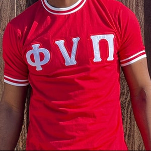 Op de afbeelding: Rood T-shirt met korte mouwen en witte afwerking rond de kraag en mouwen. Het shirt heeft een groot wit geborduurd Grieks letterontwerp dat "ΦΥΠ" luidt.
