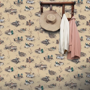 May include: A beige wallpaper with a repeating pattern of ducks swimming in a pond. A wooden coat rack with a straw hat and two jackets hanging on it is in the center of the image.