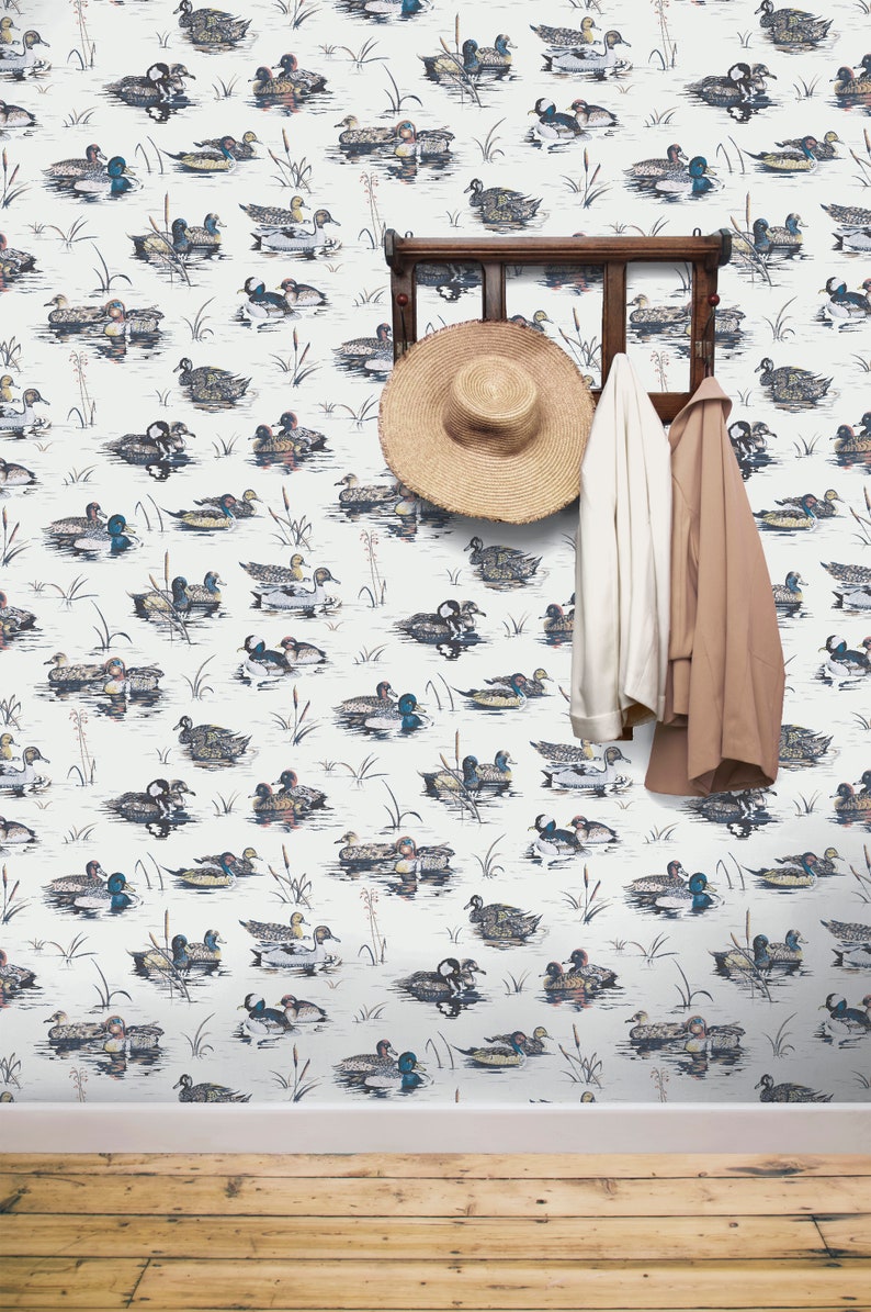 May include: White wallpaper with a repeating pattern of ducks swimming in a pond. A wooden coat rack with a straw hat and two jackets hanging on it.