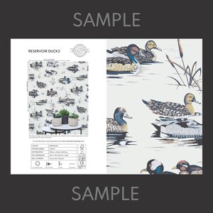 May include: A sample of "Reservoir Ducks" wallpaper featuring a white background with a repeating pattern of ducks swimming in a pond. The wallpaper is by Creative Covering and the pattern number is C100227. The pattern repeat is 53 cm (21 inches) and the roll coverage is 5.2 sq meters (56 sq ft).