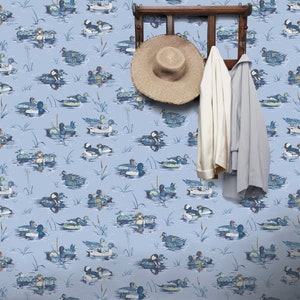 May include: Blue wallpaper with a repeating pattern of ducks swimming in a pond. The wallpaper is accented with a wooden coat rack with a straw hat and two coats hanging on it.