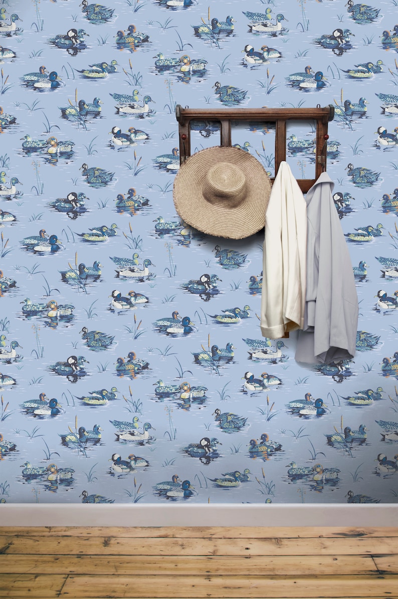 May include: Blue wallpaper with a repeating pattern of ducks swimming in a pond. The wallpaper is accented with a wooden coat rack with a straw hat and two coats hanging on it.