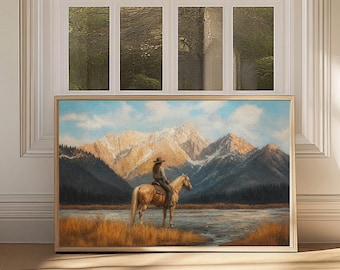 May include: A rectangular framed wall art print featuring a landscape painting of a person on horseback standing near a body of water. The scene includes golden-brown grasses in the foreground, snow-capped mountains, and a blue sky with clouds.