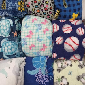 May include: A collection of various fabric items with diverse patterns. Designs include blue and white turtles, pink and blue butterflies on a checkered background, baseballs, and panda bears. Other patterns feature leopard print and the University of Michigan logo.