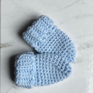 May include: A pair of light blue knitted baby booties with a textured pattern.