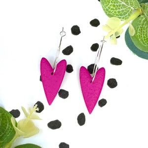 May include: A pair of pink heart-shaped hoop earrings with a textured finish. The earrings are made of polymer clay and have a silver hoop.
