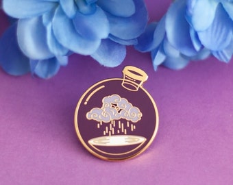 May include: A gold-colored enamel pin featuring a purple glass bottle with a cloud inside, raining down into the bottle. The pin has a gold-colored rim and a gold-colored stopper.